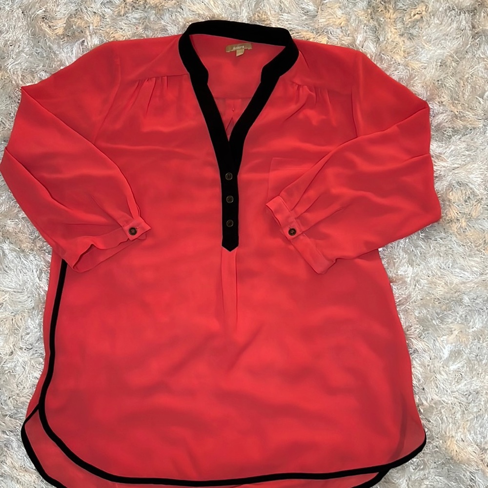 A orangey red Takara button blouse with black lining on the colors and sides.
